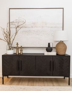 a living room with a large painting on the wall next to a black sideboard