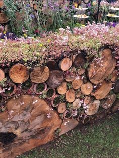 a large pile of wood sitting on top of a lush green field next to flowers