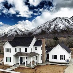 a large white house sitting in the middle of a field with snow covered mountains behind it