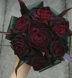 a bouquet of red roses is held by someone's hand on the sidewalk in front of them