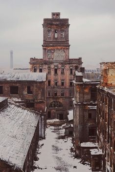 an old building with snow on the ground and buildings in the foreground, looking down at it