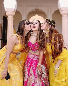 three women dressed in yellow and pink are kissing each other with their mouths wide open