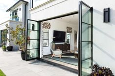 an open glass door leading to a living room and dining area with potted plants