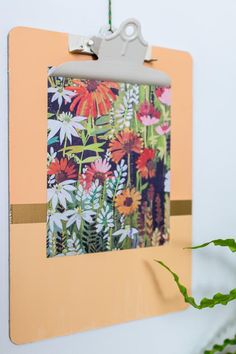 a clipboard hanging on the wall with flowers and plants in it's corner