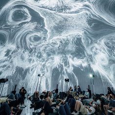 a group of people sitting on the ground in front of a large projection screen that looks like an animal's head