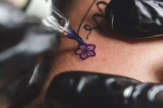 a tattoo artist working on the back of a woman's neck with blue ink