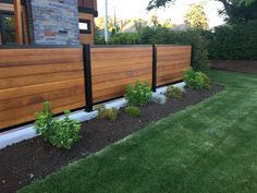 a wooden fence in front of a house with green grass and plants growing on the side