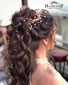 a woman with long curly hair and gold beads in her hair is seen from the back