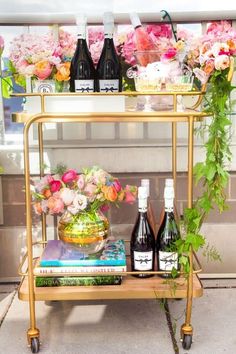 a gold bar cart with bottles of wine and flowers