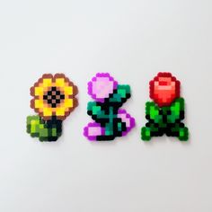 three pieces of pixel art made to look like flowers on a white surface with one flower in the middle