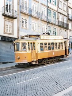 an old yellow trolley car is on the tracks in front of some buildings and people