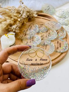 a person holding up a wine glass with two wedding rings on it and confetti sprinkles in the background