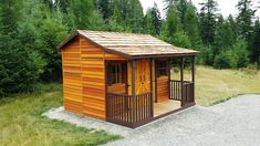 a small wooden shed sitting in the middle of a field next to some tall trees