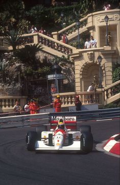 a man driving a race car down a street next to a tall building with stairs on it