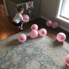 a little boy is playing with pink balloons in the middle of a room that has pig faces on them