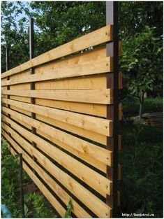 a wooden fence is shown in front of some trees and bushes, with the top section made out of wood slats