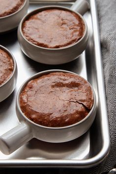 four white mugs filled with chocolate cake sitting on top of a metal pan,