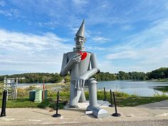 a statue of a man holding a heart in front of a body of water and trees