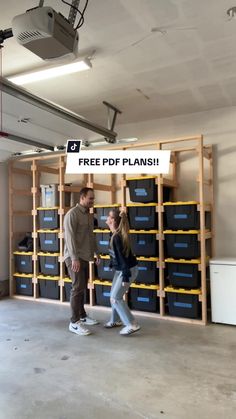 a man and woman walking in front of shelves with boxes on the wall behind them