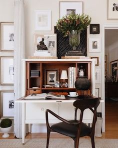 a desk with a chair, vase and pictures on the wall