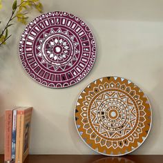 two decorative plates sitting on top of a wooden table next to a vase with flowers