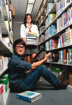 two people sitting on the floor in front of bookshelves with one person holding a book