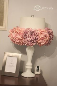 a white lamp with pink flowers on it next to a picture frame and framed photograph