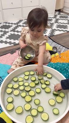 two young children are playing with cucumbers in a large bowl on the floor