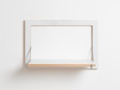 an empty white frame hanging on the wall with a wooden shelf in front of it