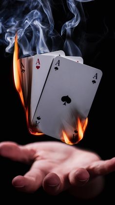 two hands holding playing cards with flames coming out of the top and on to them