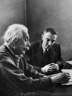 two men sitting at a table with papers in front of them and one man looking down