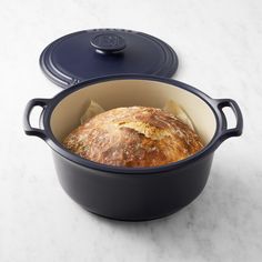 a loaf of bread in a pot on a marble countertop next to a blue lid