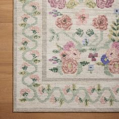 a white rug with flowers on it sitting on top of a wooden floor next to a wall