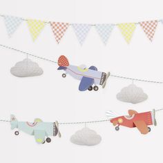 paper airplanes are hanging from a string on a white wall with bunting and flags