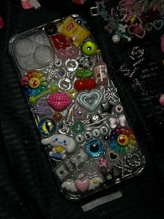 an iphone case with lots of charms and beads on the back cover, sitting on a black surface