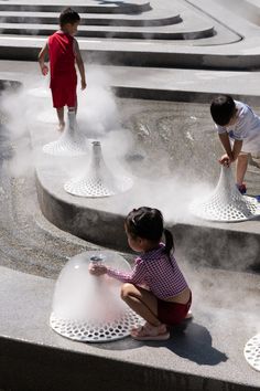 two children are playing with water in the air at an outdoor fountain that is surrounded by concrete steps