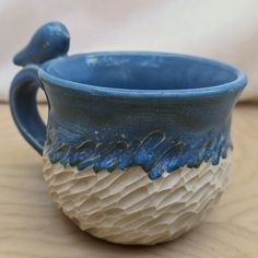 a blue and white ceramic cup sitting on top of a wooden table next to a wall