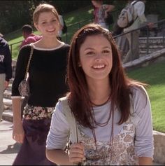 two young women walking down a sidewalk next to each other in front of some people