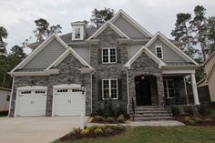 a gray brick house with white trim and two garage doors on the front door is shown