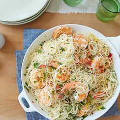 a white bowl filled with pasta and shrimp on top of a blue towel next to a wooden table