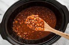 a wooden spoon in a black crock pot filled with chili and beans on a marble surface