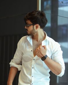 a man in white shirt and black pants standing next to a wall with his hand on his hip