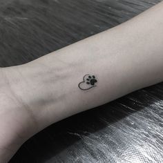 a small paw and heart tattoo on the left inner arm, with a black outline