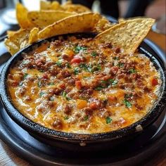 a black plate topped with a bowl of chili and tortilla chips on top of a wooden table