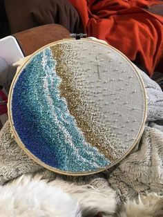 a close up of a cross stitch on a blanket with a pillow in the background