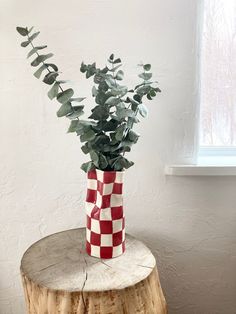 a red and white checkered vase sitting on top of a tree stump