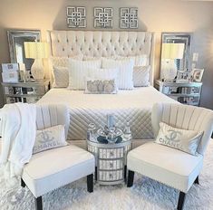 a bedroom with white bedding and two chairs in front of the bed, along with mirrors on the wall