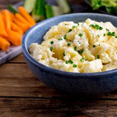 a blue bowl filled with mashed potatoes next to carrots and celery