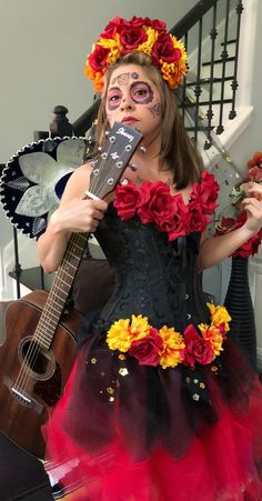 a woman with makeup and flowers on her face holding a guitar