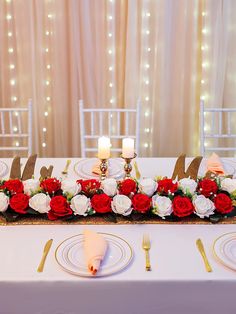 the table is set with red and white flowers, gold place settings, and candles